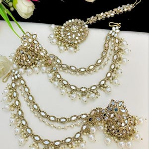 May include: A gold-toned, multi-strand hair chain with pearl accents and mirrored embellishments. The chain features a round, mirrored pendant with floral designs and a smaller, mirrored pendant with a floral design.