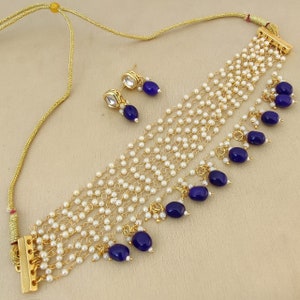 May include: A gold necklace with multiple strands of white pearls and blue gemstone accents. The necklace has a clasp closure and comes with a matching pair of earrings.