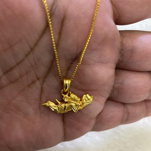 May include: A gold-colored necklace with a pendant featuring a detailed design. The pendant is suspended from a delicate chain. The necklace is displayed against a neutral background.