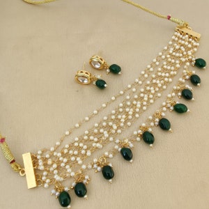 May include: A gold necklace with multiple strands of white pearls and green gemstone accents. The necklace has a clasp closure and comes with matching earrings.