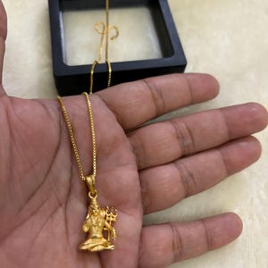 May include: A gold chain necklace with a pendant featuring a detailed depiction of the Hindu deity Shiva. The pendant is a three-dimensional representation of Shiva holding a trident.