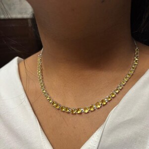 Puede incluir: Un collar de cadena de plata con piedras preciosas amarillas. El collar está puesto en el cuello de una persona.