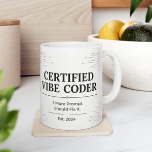 May include: A white ceramic mug featuring black text that reads CERTIFIED VIBE CODER, 1 More Prompt Should Fix It., and Est. 2024. The design includes thin black circuit board line patterns on the sides and a handle on the right side.