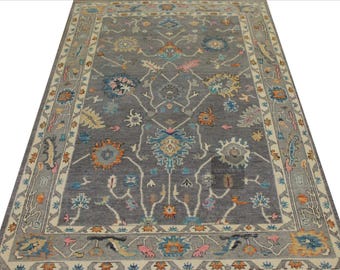 May include: A rectangular gray rug with a detailed floral pattern in shades of blue, orange, yellow, and pink. The rug has a cream-colored border with a repeating design. This rug is suitable for living rooms and bedrooms.