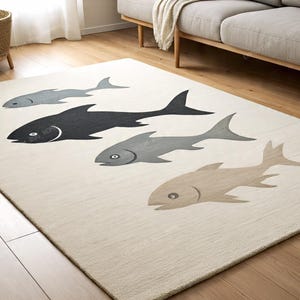May include: Beige rectangular area rug with a pattern of five stylized fish in shades of gray and black. The fish are swimming across the rug, which is placed on a hardwood floor. The rug is in a living room setting.
