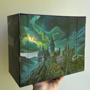 May include: A boxed set of books featuring a fantasy castle illustration. The artwork depicts a nighttime scene with a crescent moon, stars, and a castle on a rocky cliff. The box is dark with a vertical wood grain design.