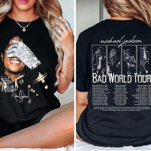 May include: A black t-shirt featuring a graphic of Michael Jackson wearing a sequined glove on the front. The back displays four black and white concert photos, the text "michael jackson BAD WORLD TOUR," and a list of tour dates and locations.
