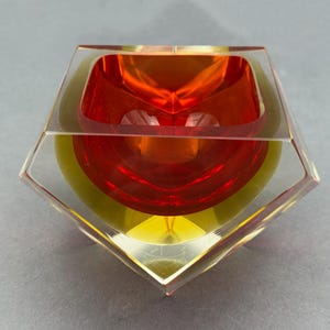 以下が含まれることがあります： 層状のデザインが施された、透明な幾何学的なボウル。ボウルは、赤い内側、黄色のミドルセクション、透明な外側という鮮やかな配色が特徴です。ボウルの形状は多角形です。