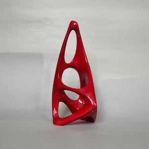 Puede incluir: Una escultura abstracta roja vibrante con un acabado brillante. La escultura tiene forma triangular con múltiples aberturas ovaladas y curvas. El diseño es moderno y llamativo, adecuado para la decoración del hogar.
