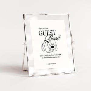 Puede incluir: Un cartel blanco con texto negro que dice "Por favor, firme nuestro LIBRO DE VISITAS" con una ilustraci&oacute;n en blanco y negro de una c&aacute;mara. El texto debajo de la c&aacute;mara dice "&iexcl;Toma una foto y deja un mensaje para recordar este d&iacute;a especial!" y "Hailey & Tristan".