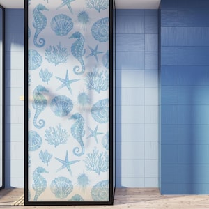 Könnte beinhalten: Eine Glastür für die Dusche mit einem sich wiederholenden Muster aus hellblauen Seepferdchen, Seesternen, Muscheln und Korallen auf weißem Hintergrund. Die Tür ist schwarz umrahmt und steht neben blau gefliesten Wänden.
