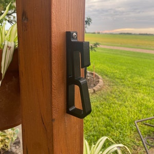 May include: A black plastic hook mounted on a wooden post. The hook has a unique design with multiple slots and a curved top.