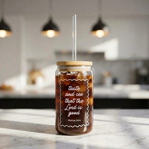 May include: A clear glass tumbler filled with iced coffee, featuring a bamboo lid and a clear glass straw. The tumbler has white text that reads "taste and see that the Lord is good" with "PSALM 34:8" below. The tumbler is on a marble surface.