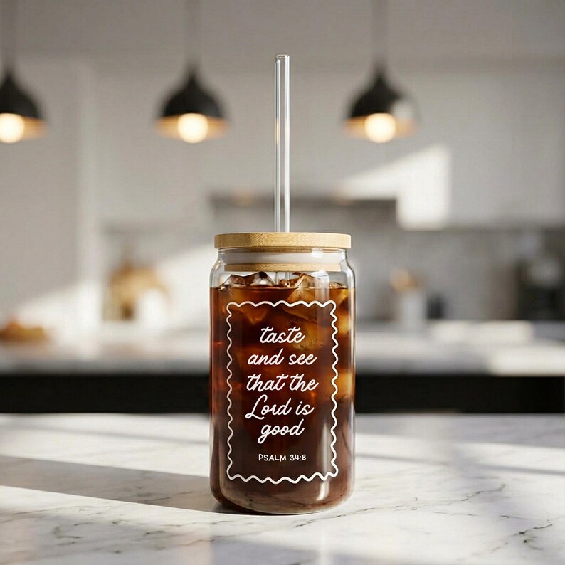 May include: A clear glass tumbler filled with iced coffee, featuring a bamboo lid and a clear glass straw. The tumbler has white text that reads "taste and see that the Lord is good" with "PSALM 34:8" below. The tumbler is on a marble surface.