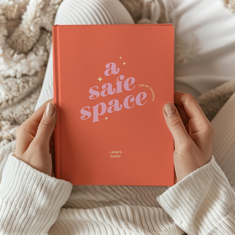 May include: Coral-colored journal with the words "a safe space" in a stylized font. The phrase "for my thoughts" is also visible. The journal is labeled "Lana's Diary".