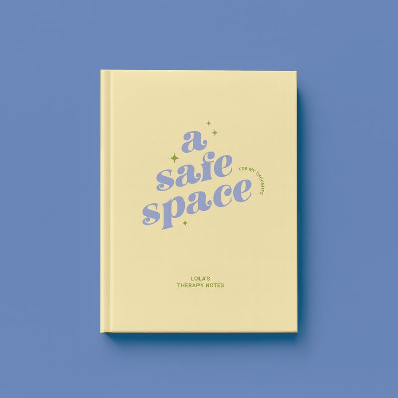 May include: A soft yellow journal with the words "a safe space" in light blue script. The journal also has the text "for my thoughts" and "Lola's Therapy Notes" in a smaller font. The journal is on a blue background.
