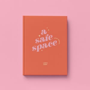 May include: An orange journal with the words "a safe space" in a cursive font. The journal also has the text "for my thoughts" and "Lana's Diary". The background is a solid pink color.