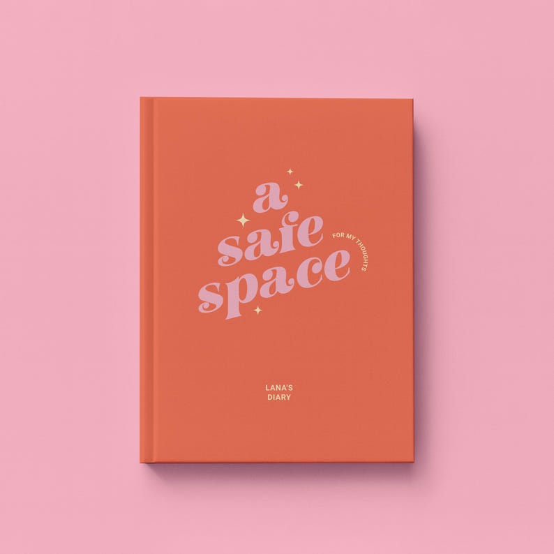 May include: An orange journal with the words "a safe space" in a cursive font. The journal also has the text "for my thoughts" and "Lana's Diary". The background is a solid pink color.
