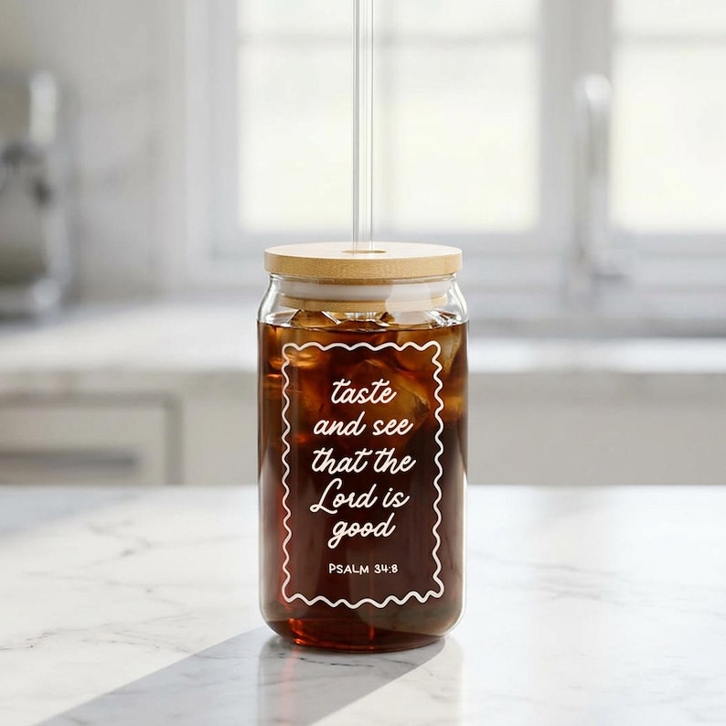 May include: A clear glass jar with a wooden lid and a clear straw, filled with a dark liquid. The jar has white text that reads "taste and see that the Lord is good" with "PSALM 34:8" below. The jar is on a white surface.