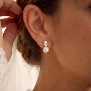 May include: A drop earring featuring a small, clear, oval-cut gemstone set above a single, round, white pearl. The earring is secured to the earlobe with a metal post. The text HandmadeByCozyah is visible in the bottom right corner of the image.
