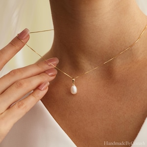May include: A delicate gold chain necklace featuring a single teardrop-shaped white pearl pendant. The necklace is secured with a simple gold bail connecting the pearl to the thin, polished gold box chain that rests against the collarbone area.