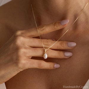 May include: A delicate gold chain necklace featuring a single, teardrop-shaped white pearl pendant. The pendant is suspended from a simple gold bail, creating a refined and understated piece of jewellery that rests against the collarbone area.
