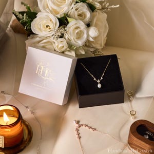 May include: A gold-toned necklace with a single teardrop pearl pendant and leaf-shaped accents, presented in a black box next to a white box with the gold text Handmade By Cozayh. The set includes matching pearl earrings and a delicate chain.