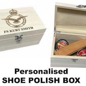 Könnte beinhalten: Eine hellfarbene Schuhputzbox aus Holz mit Scharnierdeckel und Metallverschluss. Der Deckel ist mit einem Wappen und dem Text "FS KURT SMITH" graviert. Im Inneren befinden sich zwei Schuhcremedosen und ein Holzapplikator.