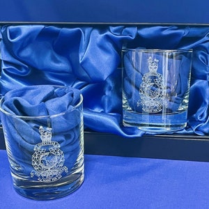 May include: Two clear glass tumblers with a blue satin lining in a navy blue box. The tumblers are engraved with the Royal Gibraltar Regiment crest, which includes a crown, a globe, and the words "Gibraltar" and "Pro Mari Per Fide."
