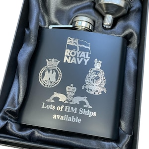 May include: A matte black metal flask featuring an engraved Royal Navy emblem, two ship crests, and the text "Lots of HM Ships available." The flask includes a silver-toned screw cap and a matching metal funnel, all presented in a black box.