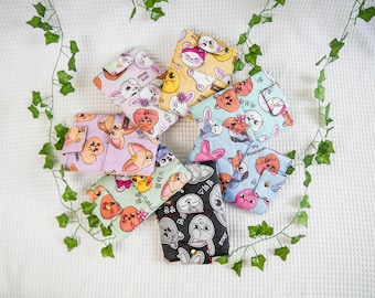 May include: A collection of eight small, rectangular, quilted fabric pouches featuring colorful cartoon character prints and Korean text. Each pouch is secured with a gold-toned metal snap button and displays various animal-like faces in pastel and bold colors.