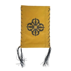May include: A yellow fabric pouch with black tassels and a black printed symbol. The symbol is a stylized mandala with a circle in the center.