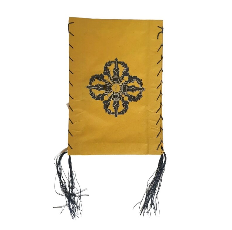 May include: A yellow fabric pouch with black tassels and a black printed symbol. The symbol is a stylized mandala with a circle in the center.