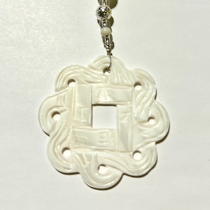 May include: Ivory pendant necklace with a carved floral design. The pendant has a square centre and is surrounded by a decorative, swirling pattern. The necklace features a silver chain and small, round beads.
