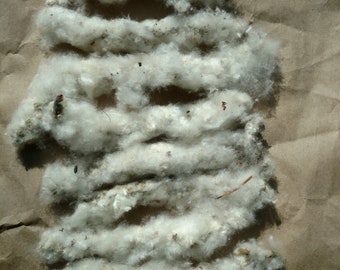May include: A close-up of a pile of white fluffy cotton fibers on a brown paper background.