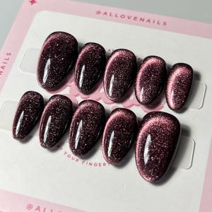 Könnte beinhalten: Ein Set oval geformter Kunstnägel in tiefem Burgunderrot mit Glitzereffekt. Die Nägel sind auf einer rosa Karte mit dem Text "@ALLOVENAILS" und "YOUR FINGER" angeordnet.