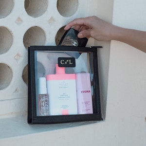 Puede incluir: Una bolsa negra con cremallera transparente con las letras "C x L" en letras doradas. La bolsa contiene una botella rosa con el texto "Body Lotion Lotion pour le corps" y un tubo rosa con el texto "BYOMA MOISTURIZING GEL CREAM". También hay una pequeña botella marrón con el texto "62%  PLUM & SALICYLIC ACID  POTASSIUM & CAFFEINE".