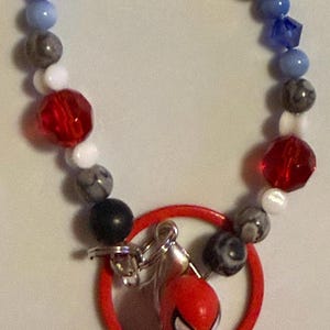 May include: A Spidey-themed keychain featuring a red Spider-Man figure, a red ring, and a beaded bracelet. The bracelet has beads in various colors, including blue, white, gray, and red, with the name "SPIDEY" spelled out.