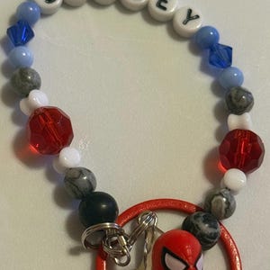 May include: A beaded bracelet with the name "SPIDEY" spelled out in white letter beads. The bracelet features blue, gray, red, and white beads, and a red Spider-Man charm.