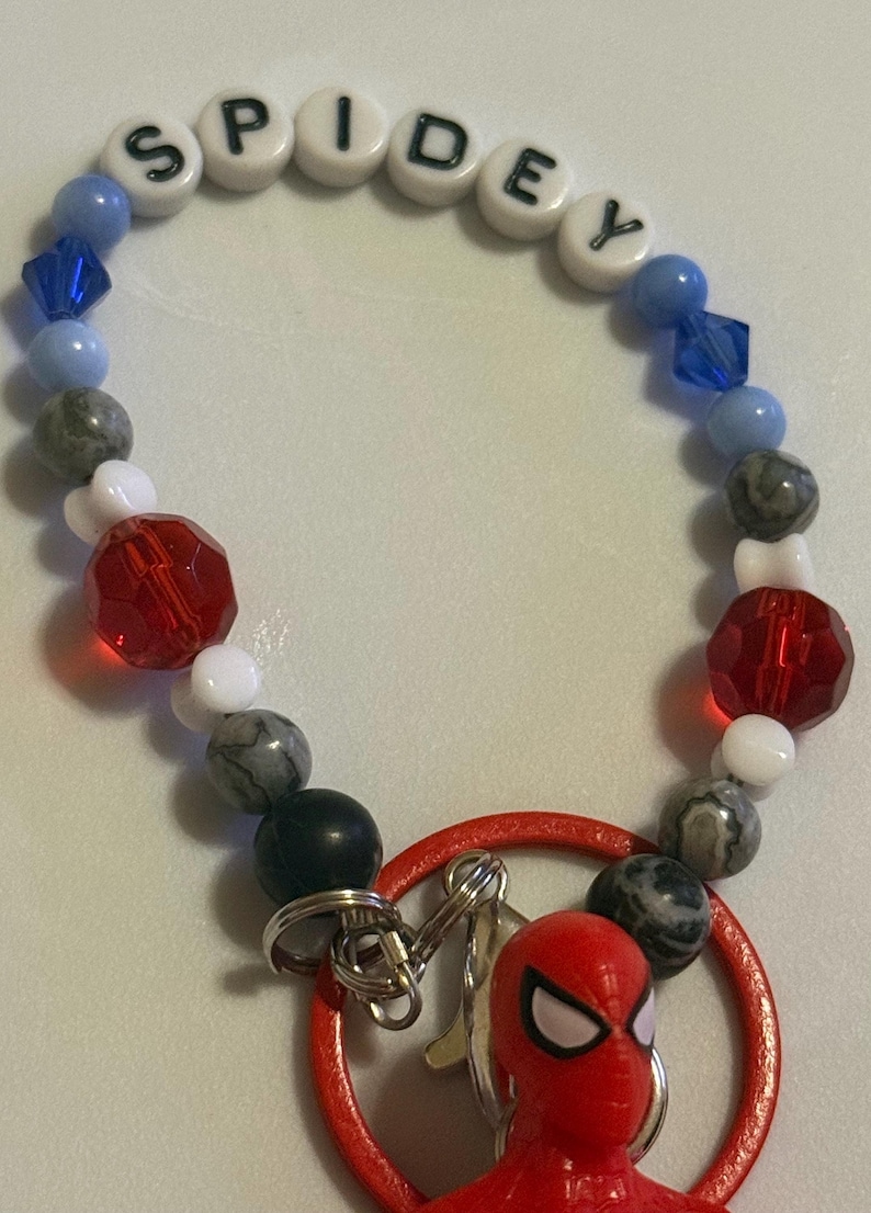 May include: A beaded bracelet with the name "SPIDEY" spelled out in white letter beads. The bracelet features blue, gray, red, and white beads, and a red Spider-Man charm.