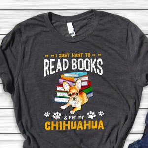 May include: A dark gray t-shirt with the text "I just want to read books & pet my chihuahua" in yellow and white. A chihuahua is sitting on a stack of books.