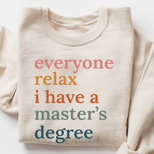 May include: A beige sweatshirt with the text "everyone relax i have a master's degree" printed in rainbow colors.