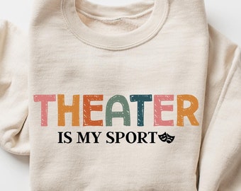 May include: A beige sweatshirt with the text "THEATER IS MY SPORT" in colorful letters and two black masks.