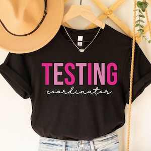 May include: Black t-shirt with the text "TESTING coordinator" in pink and purple lettering.