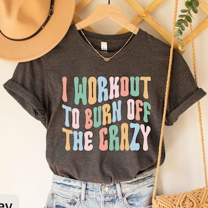 May include: Dark grey heather t-shirt with the text "I workout to burn off the crazy" in colorful letters.