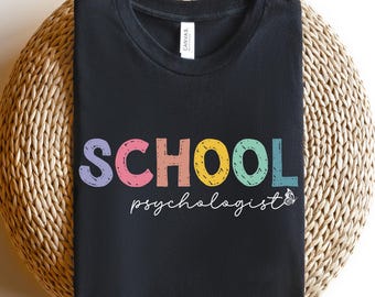 May include: Black t-shirt with the text "SCHOOL psychologist" in rainbow colors. The word "SCHOOL" is in large, colorful letters with a small butterfly graphic next to the text.