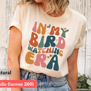 May include: A natural colored Bella Canvas 3001 t-shirt with the text "In My Bird Watching Era" in a colorful retro font.