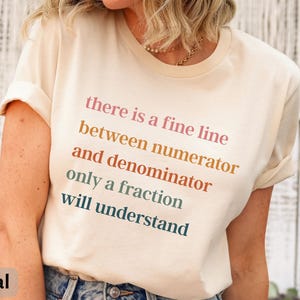 May include: A white t-shirt with a humorous math-themed quote in rainbow colors: "there is a fine line between numerator and denominator only a fraction will understand".