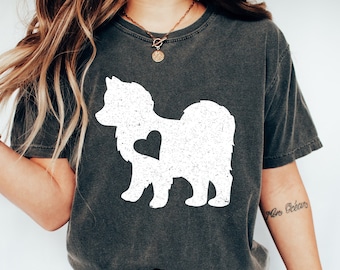 Può includere: T-shirt grigio scuro con grafica bianca invecchiata di un cane con un cuore. La maglietta ha girocollo e maniche corte. La grafica del cane è centrata sul davanti. La maglietta è realizzata in un materiale morbido e confortevole.