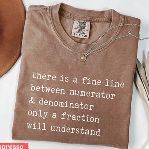 May include: Espresso brown t-shirt with a white graphic that reads "there is a fine line between numerator & denominator only a fraction will understand".